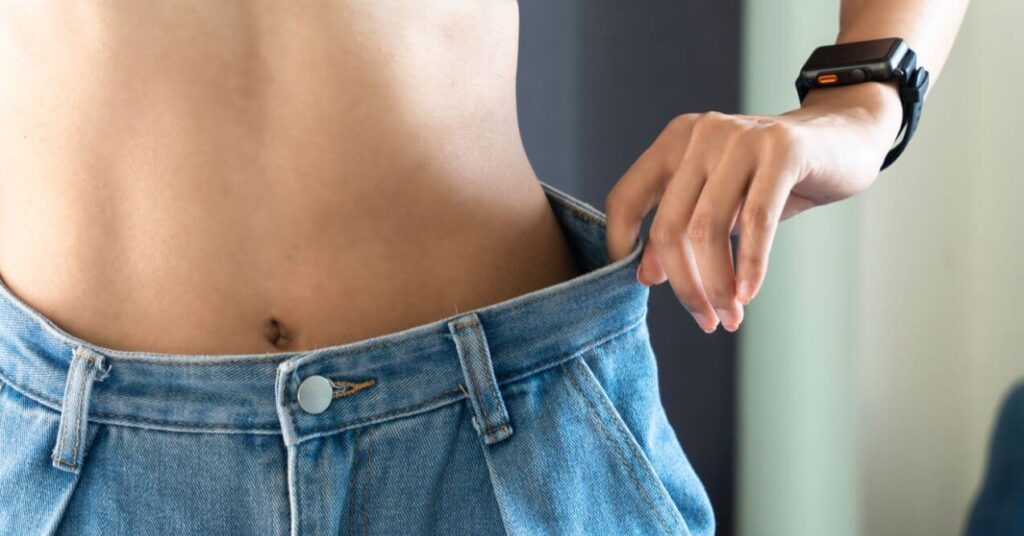 Person showing significant weight loss by pulling on loose jeans.