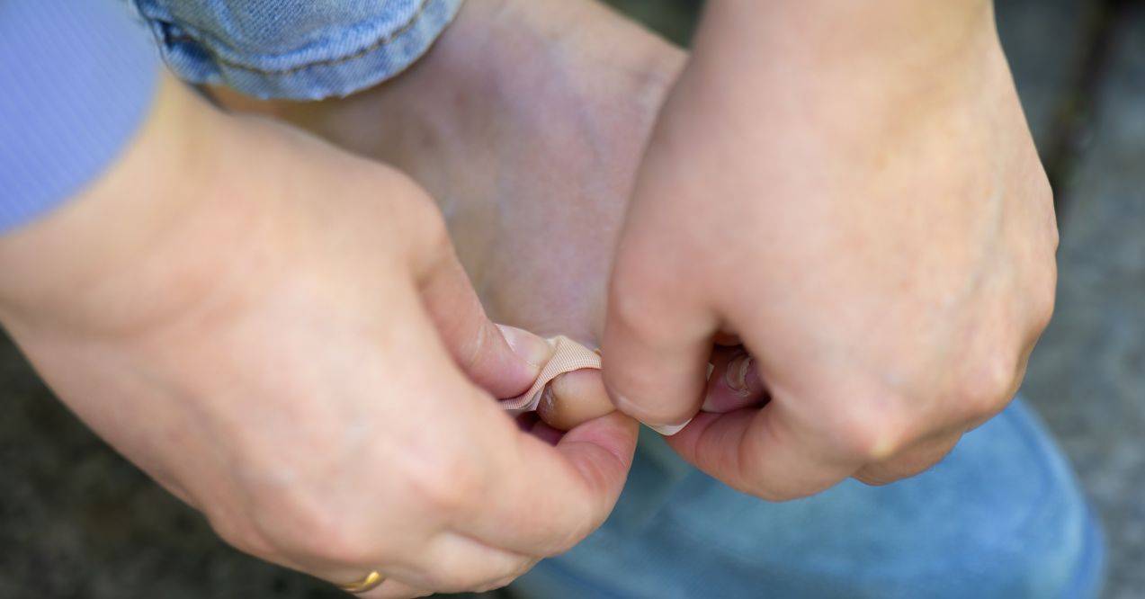 A close-up of hands applying a small bandage to a toe, treating a minor foot injury.