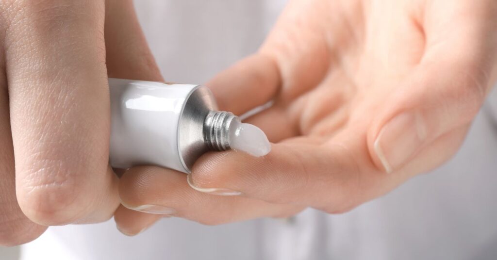 A close-up of a hand squeezing a small amount of antibiotic ointment from a tube onto fingers