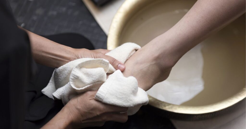 A healthcare worker wearing gloves gently washes the foot of a person, providing foot care.