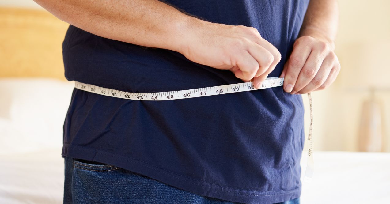 Close-up of a person measuring their waist with a tape measure, indicating weight gain or monitoring body measurements.