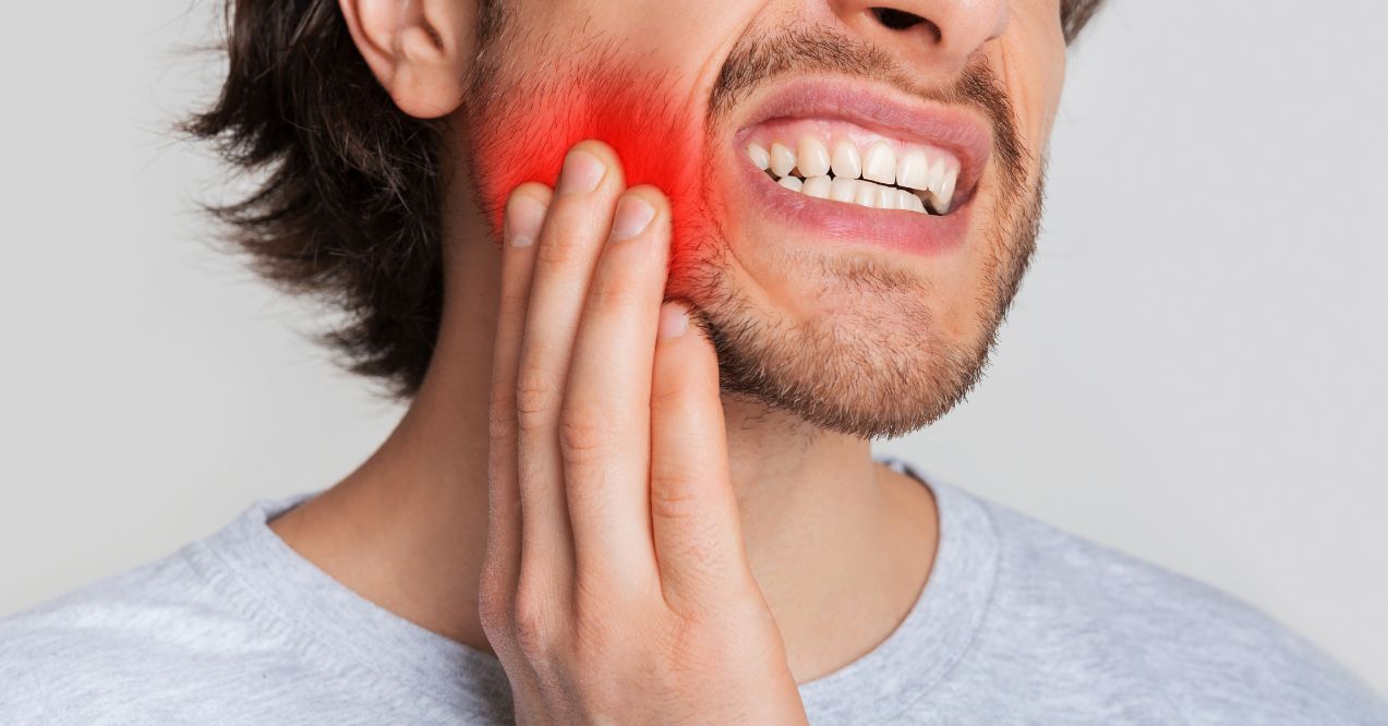 A man holding his jaw in pain, questioning can a tooth infection cause swollen lymph nodes.