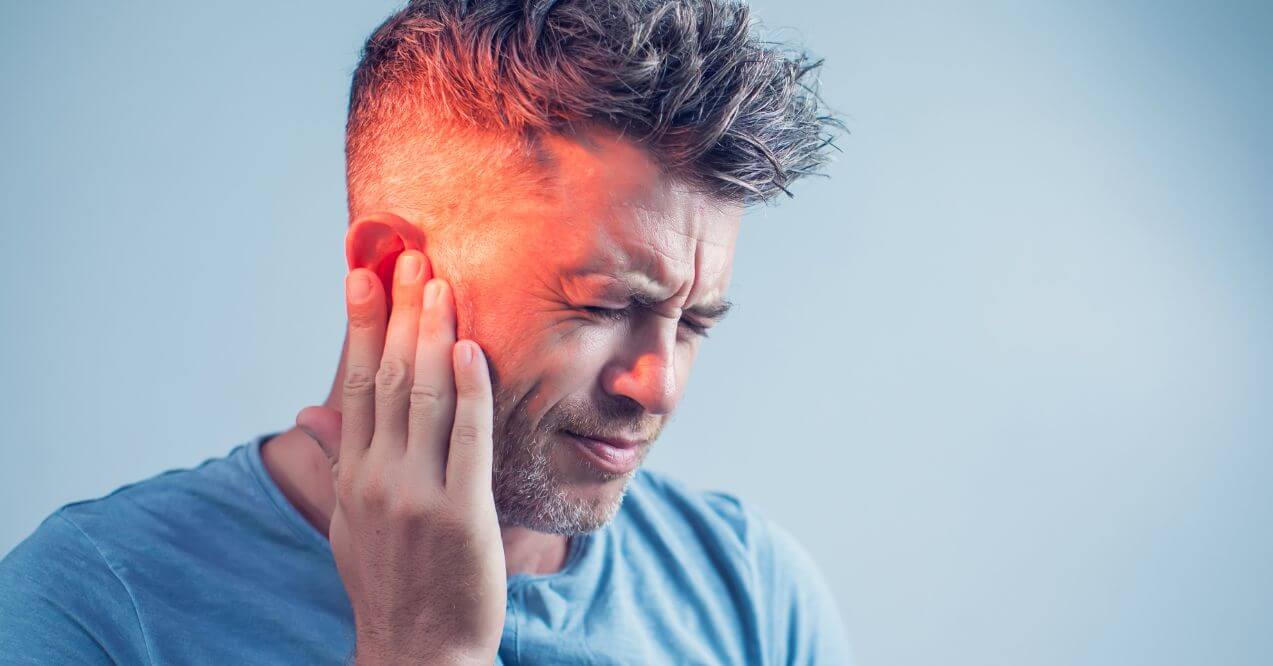 Man holding his ear with a pained expression, possibly due to an ear infection.