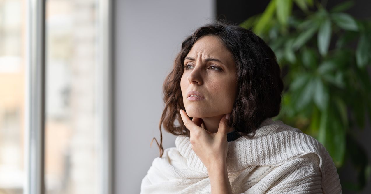 A woman touching her neck, possibly checking for enlarged preauricular lymph nodes.