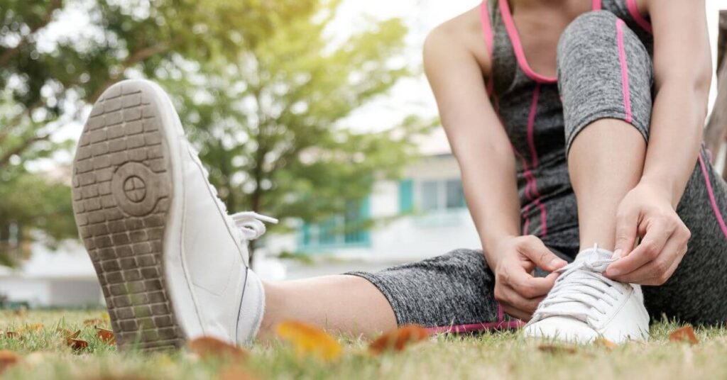 Person in athletic wear tying shoelaces while sitting on the grass, preparing for outdoor exercise.