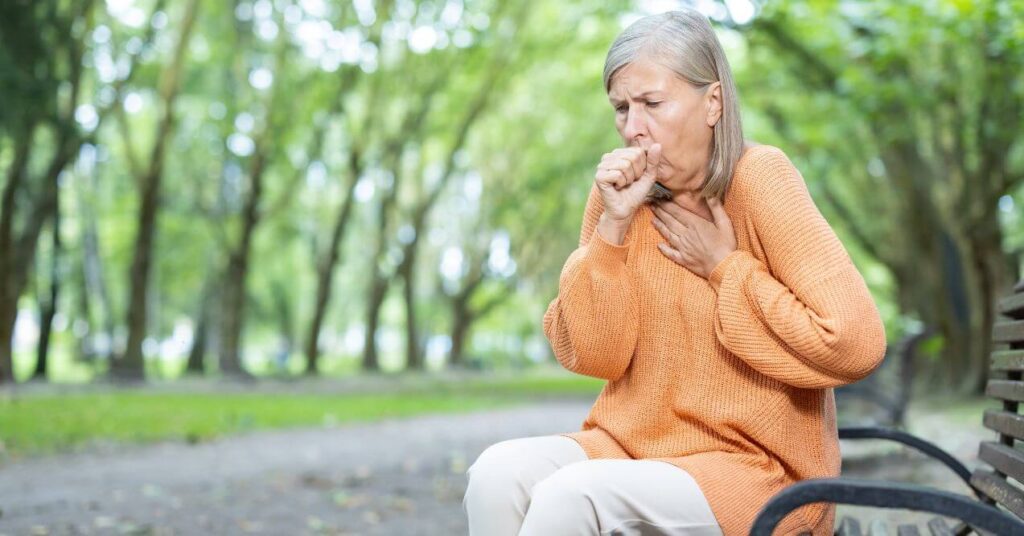 Elderly woman coughing while sitting on a park bench