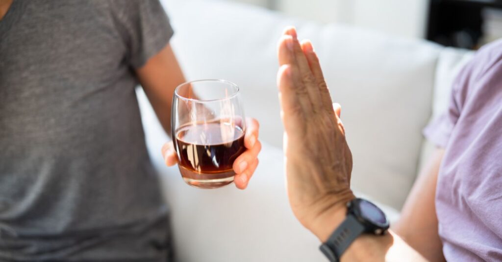 Person holding up their hand to refuse a glass of alcohol being offered.