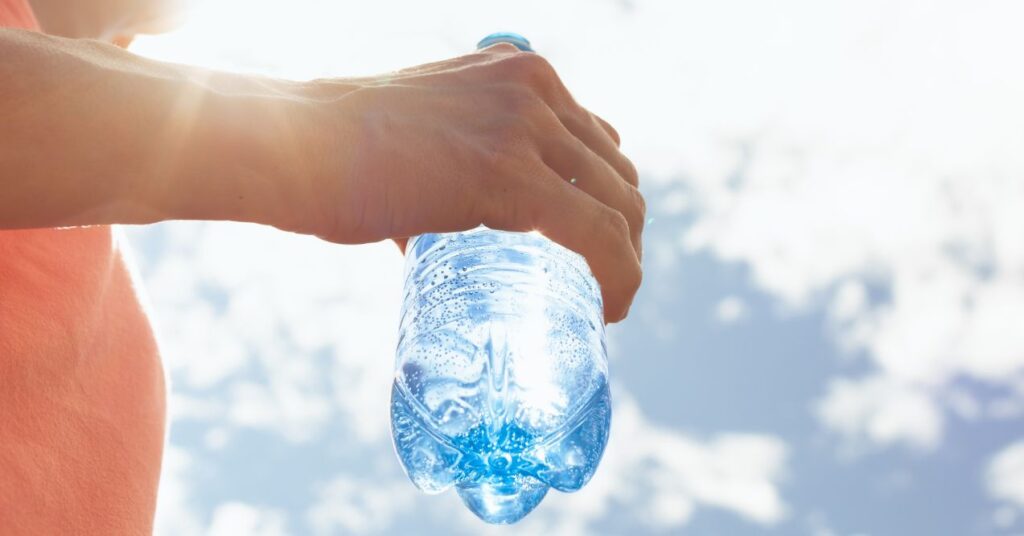 Hand holding a clear plastic water bottle with the sun shining in the background.