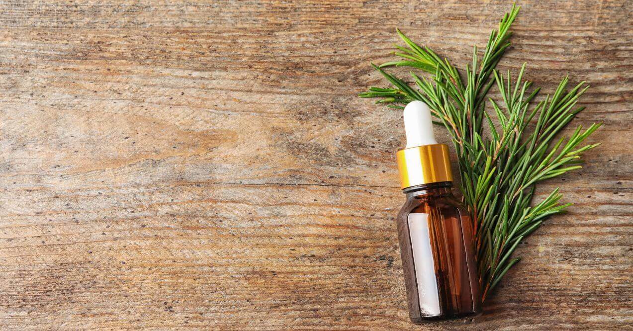 A dropper bottle of tea tree oil next to fresh rosemary.