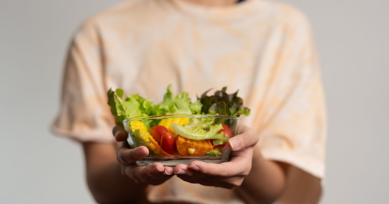 A bowl of fresh mixed vegetables including lettuce, tomatoes, and bell peppers being held by a person.