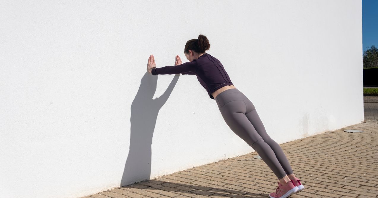 Woman performing wall presses outdoors as part of a somatic exercise routine.