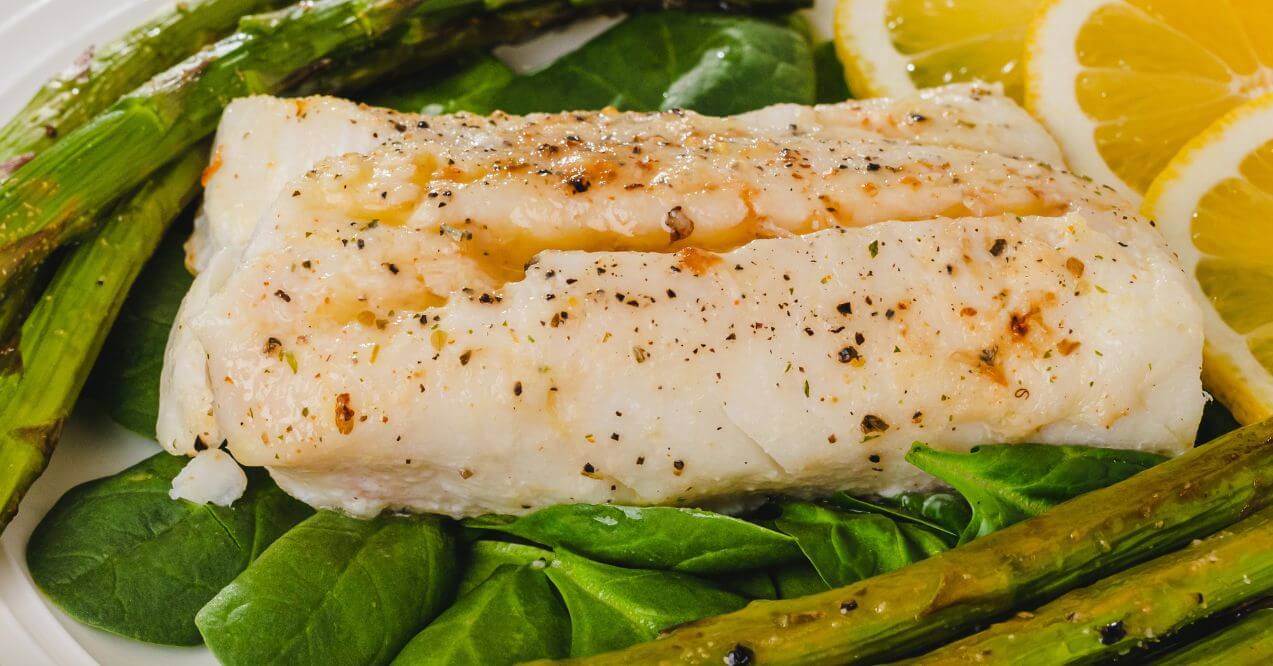 A dish of baked cod served with asparagus and lemon slices.