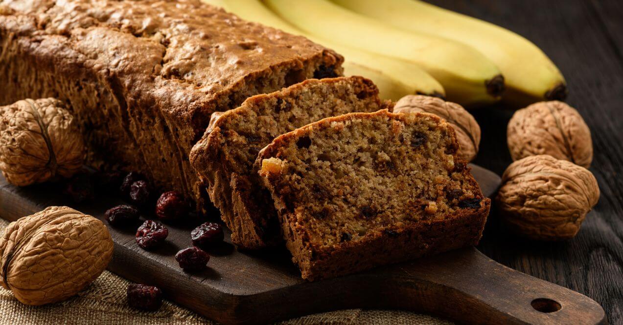 Freshly baked banana bread with walnuts, surrounded by bananas and walnuts.