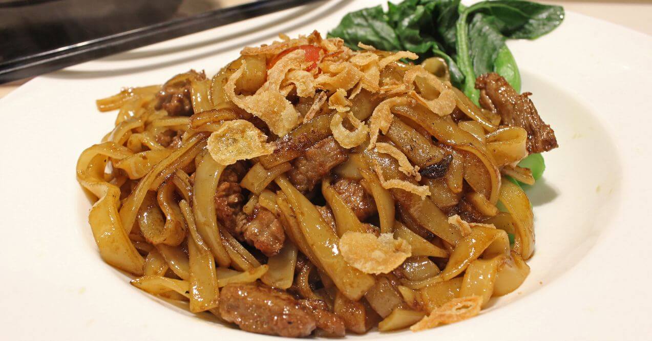 A plate of stir-fried beef with rice noodles and fresh vegetables.