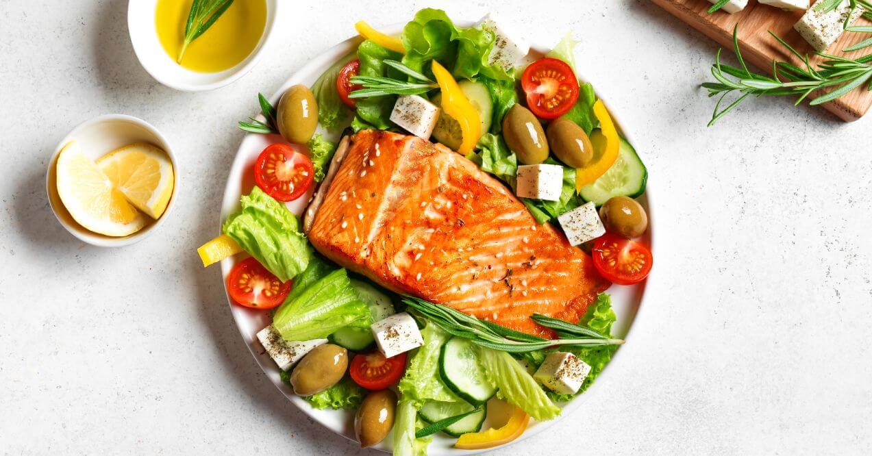 A plate of grilled salmon served with fresh salad and tomatoes.