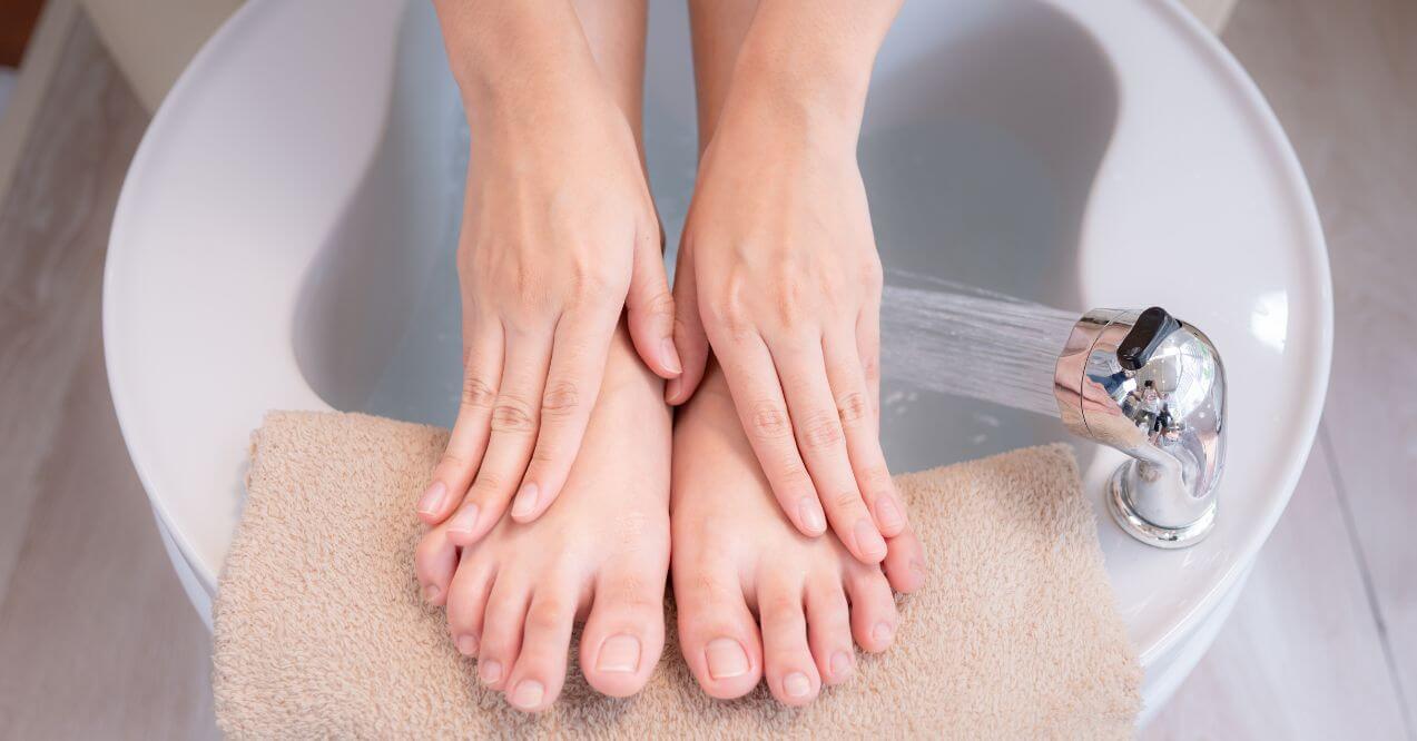 Hands resting on clean feet during a foot soak in a basin for home remedies.