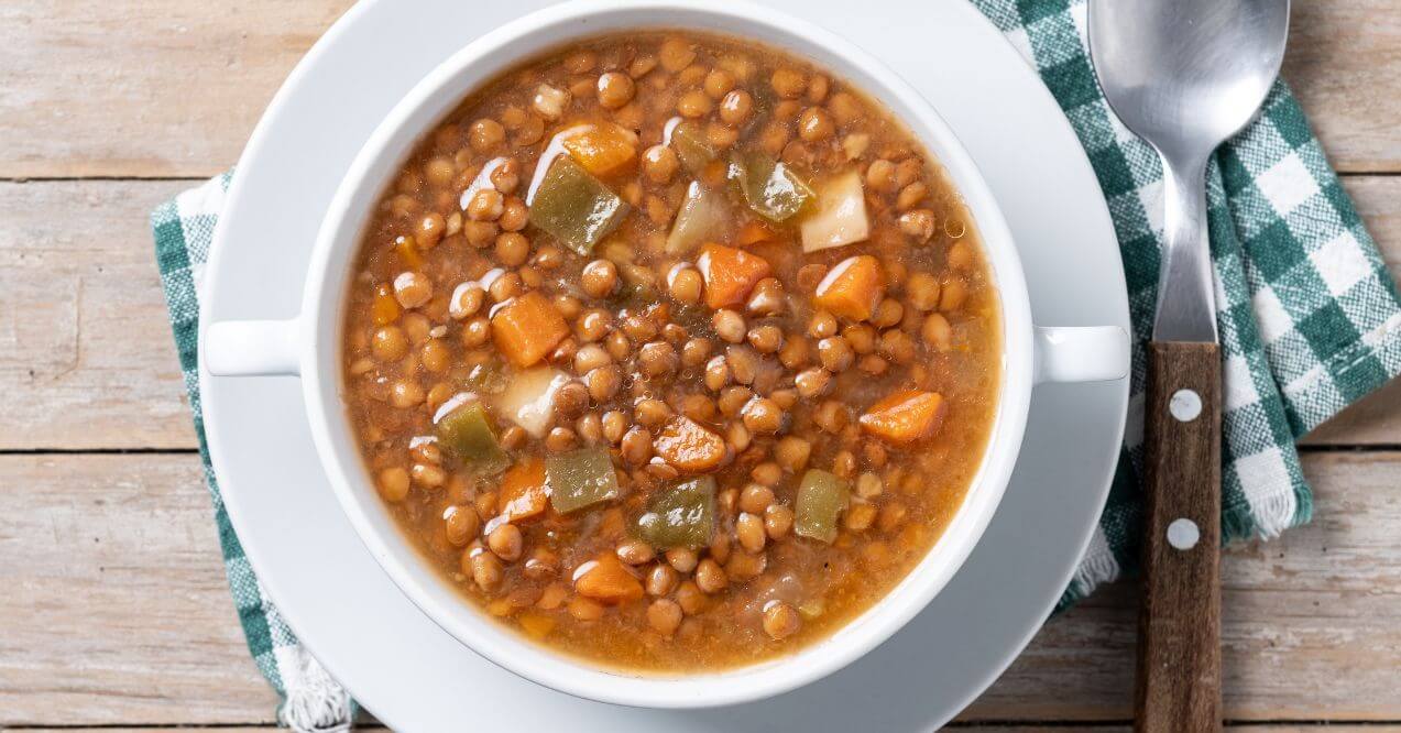 Bowl of lentil soup with carrots, celery, and peppers on a wooden table.