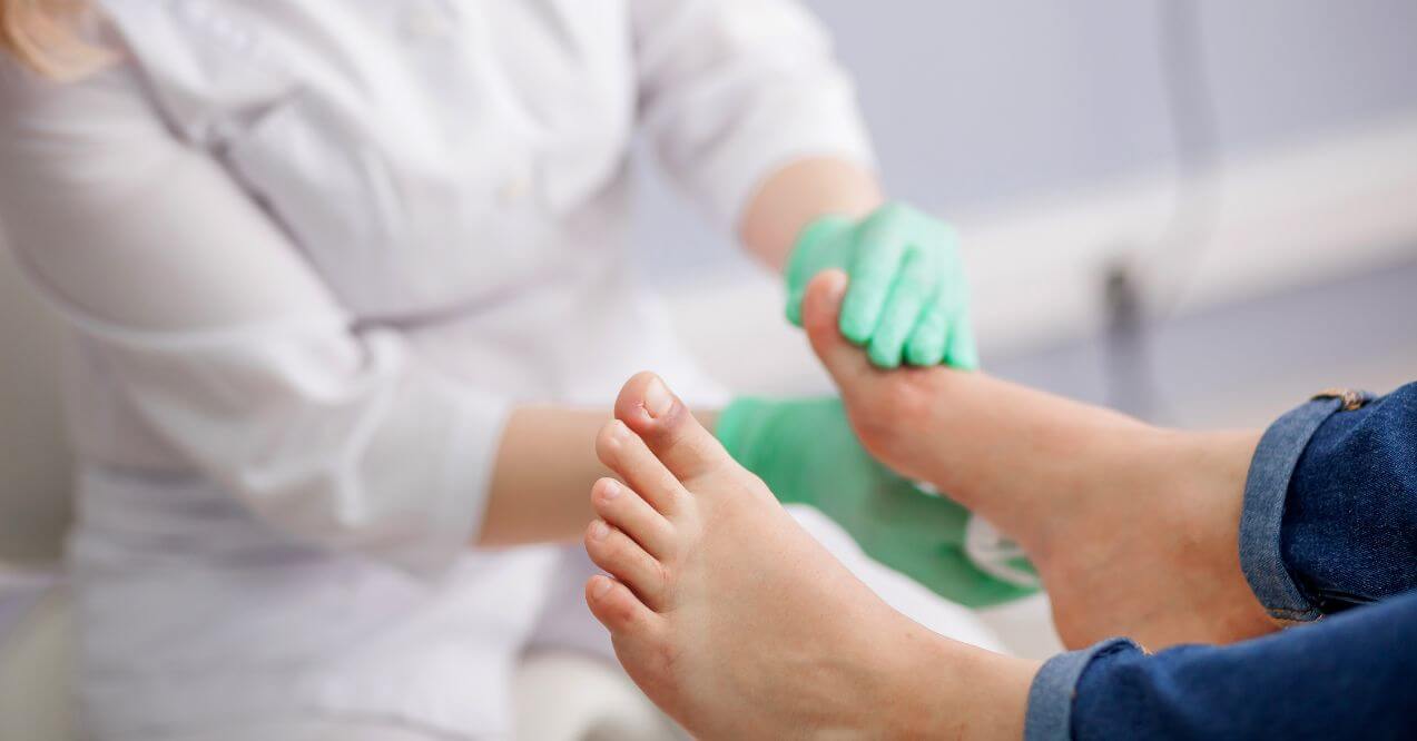 Medical professional wearing gloves examining a person's feet.