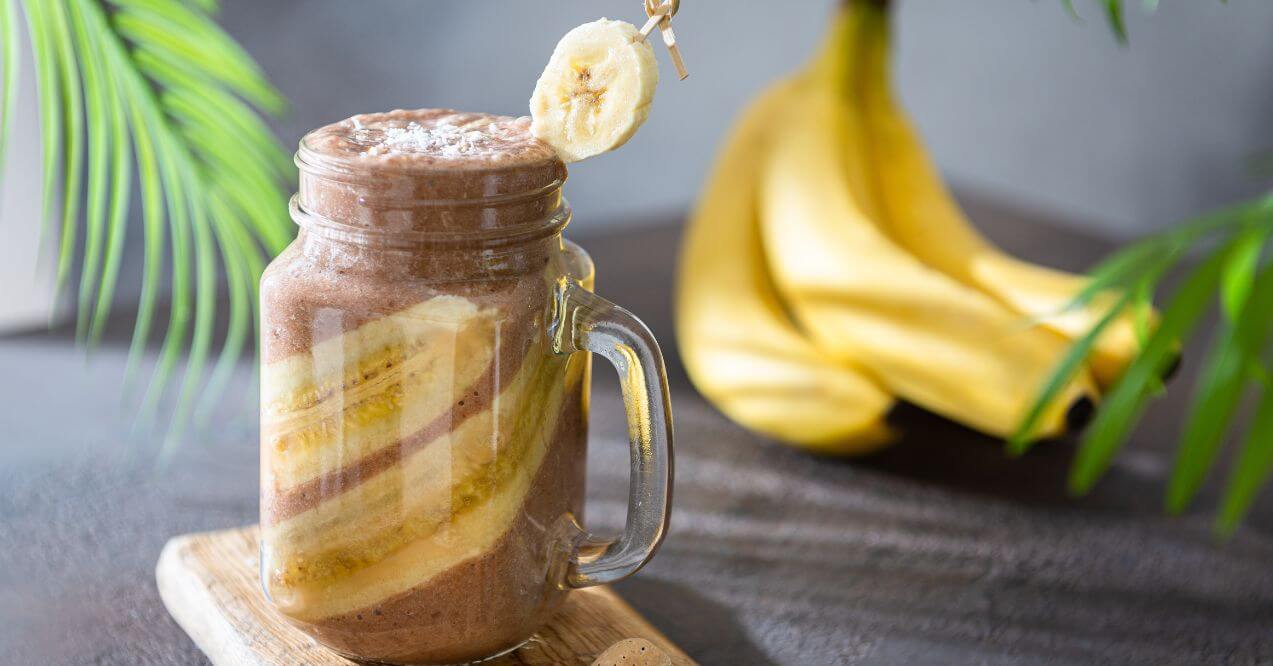 Chocolate banana smoothie in a jar, topped with a banana slice and fresh bananas.