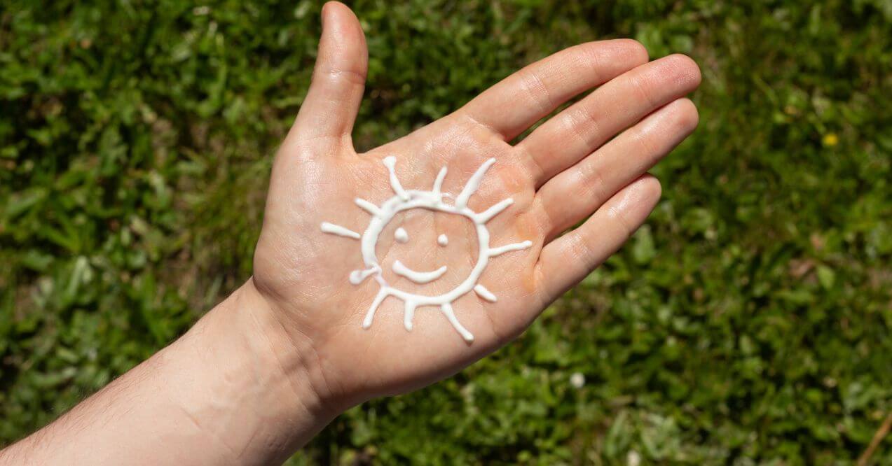 Sunscreen in the shape of a sun on a person's palm against a green grass background.