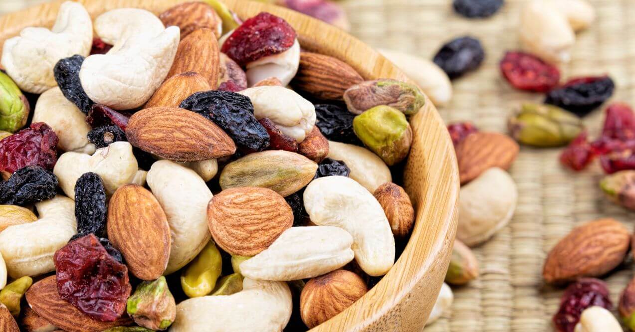 Trail mix with almonds, cashews, pistachios, and dried cranberries in a wooden bowl.