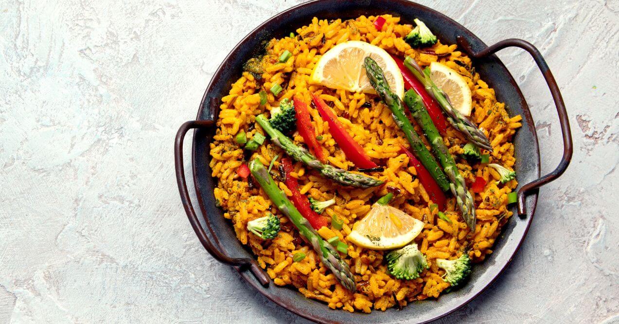 Colorful vegetable paella with saffron rice, asparagus, peppers, and lemon slices.