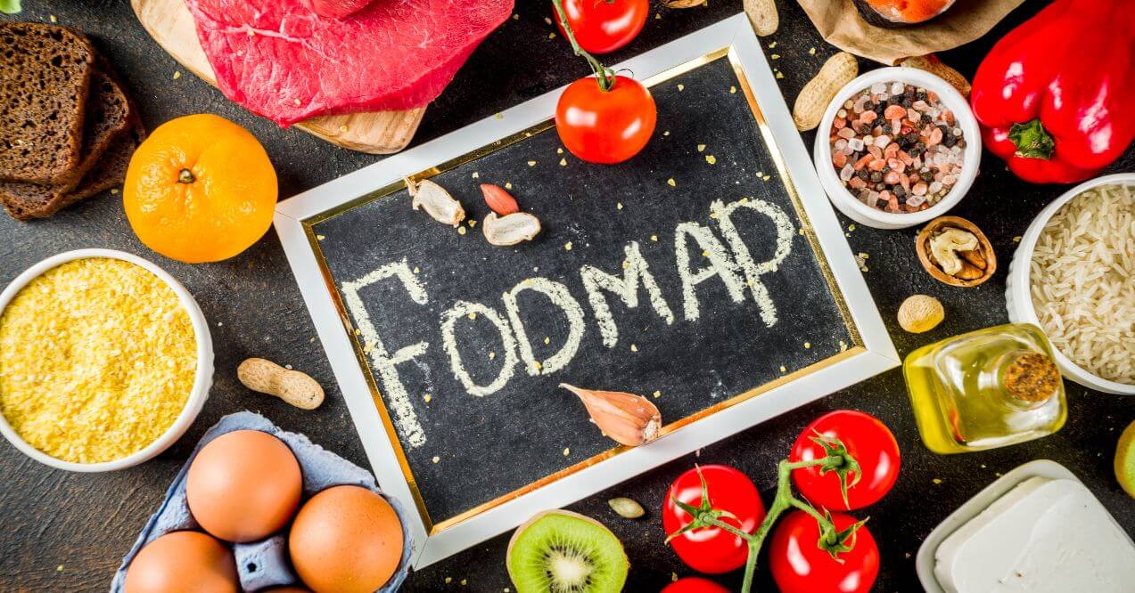 Low FODMAP diet recipes chalkboard surrounded by fresh ingredients like tomatoes, rice, and eggs.