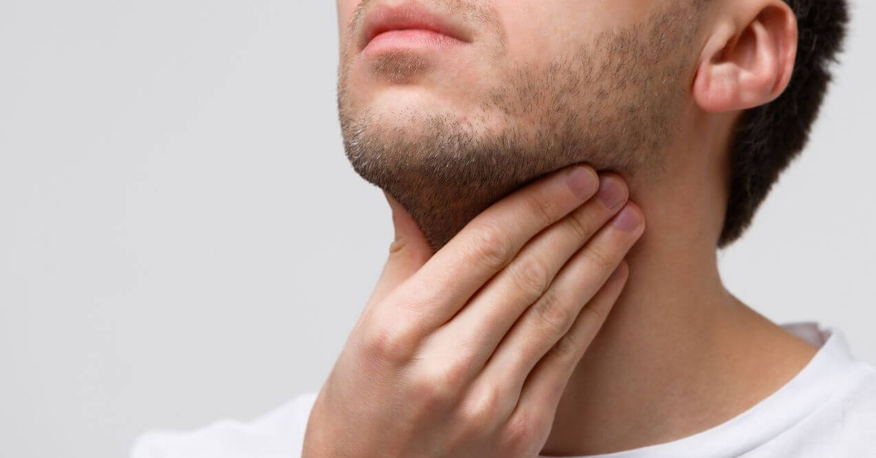 Man touching his neck near the jaw, indicating possible discomfort or a lump on jawline.