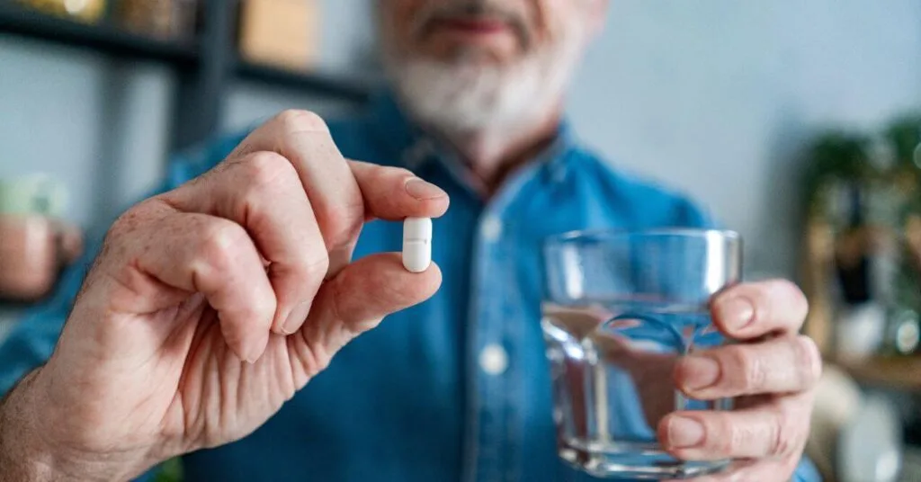 Senior man holding a white capsule and a glass of water