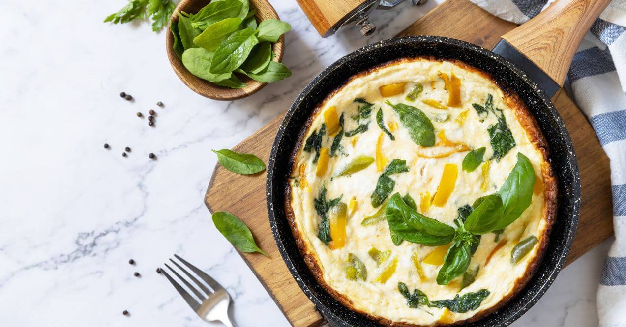 Spinach and bell pepper scrambled eggs in a skillet with fresh basil and parsley.