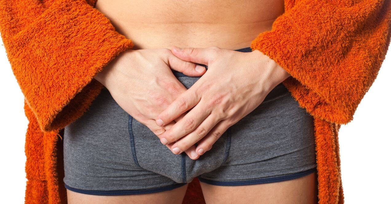 Man in underwear holding his groin with both hands