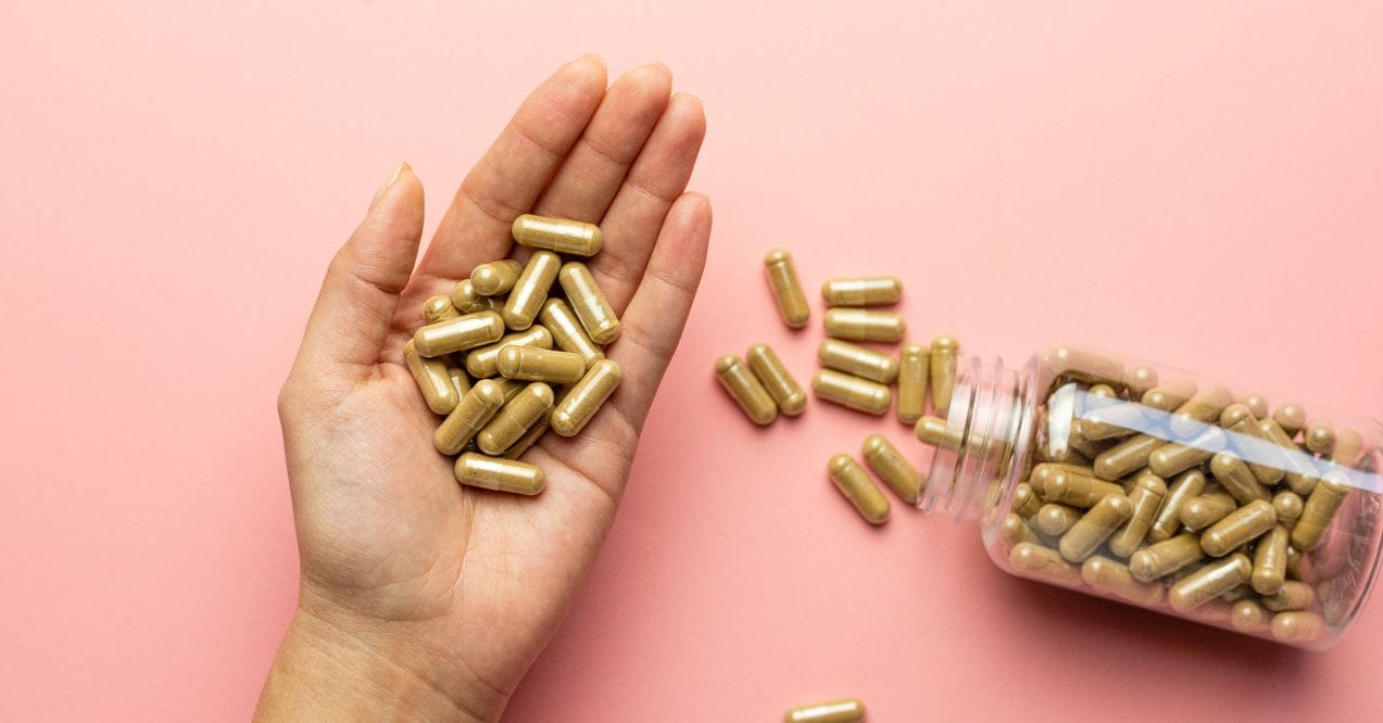 Hand holding ashwagandha capsules with a bottle on a pink background