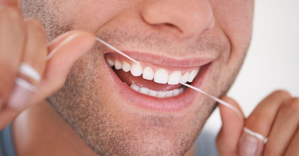 Smiling man flossing his teeth as part of maintaining good oral hygiene.