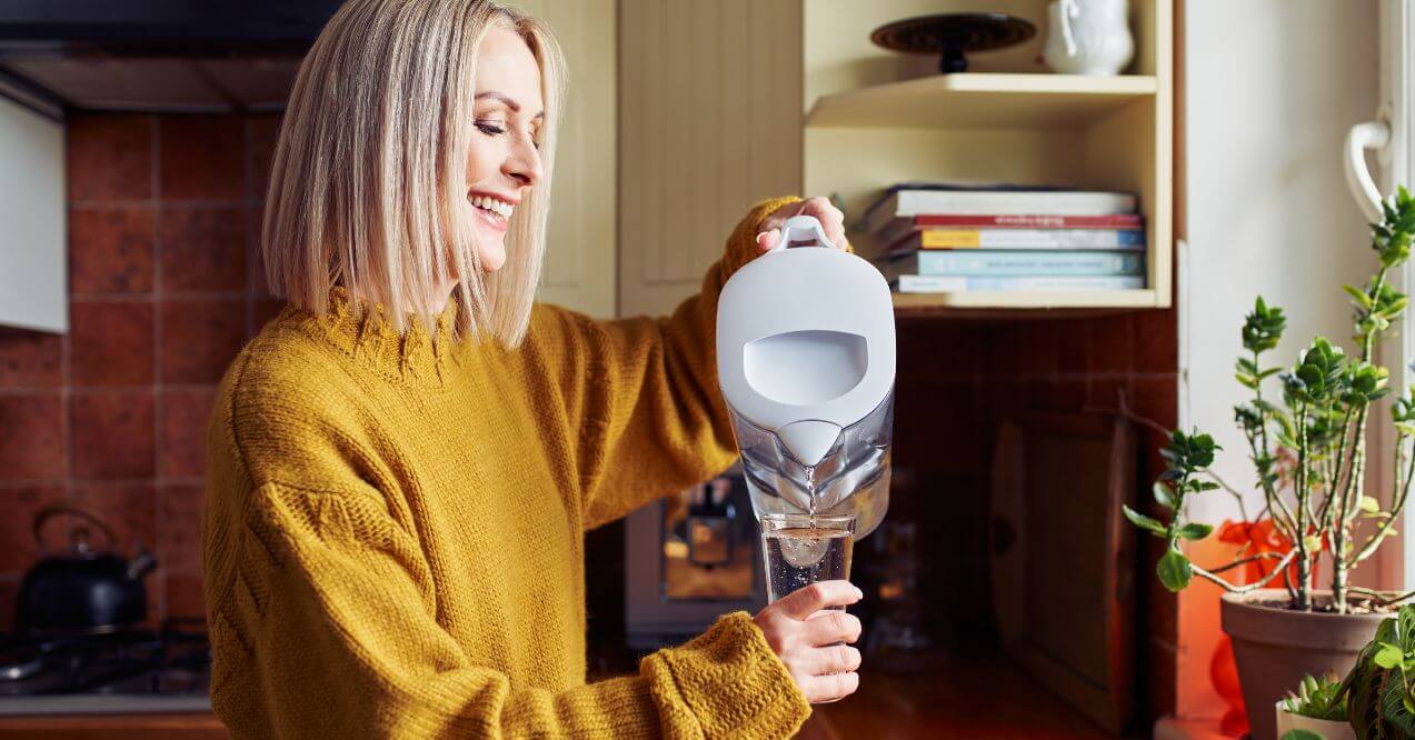 Woman pouring water from a filter jug in kitchen.