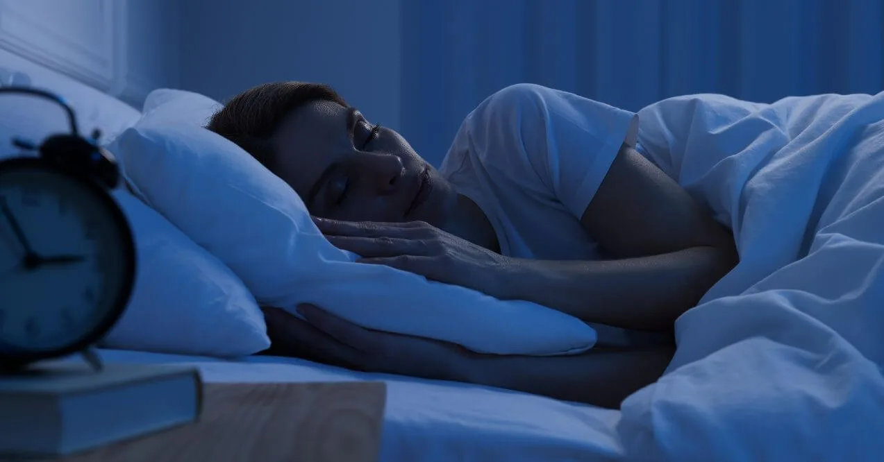 Woman sleeping peacefully on a pillow in a dimly lit room with an alarm clock nearby.