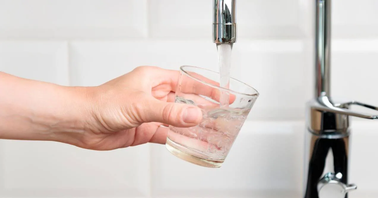 Hand holding a glass of water being filled from a faucet.