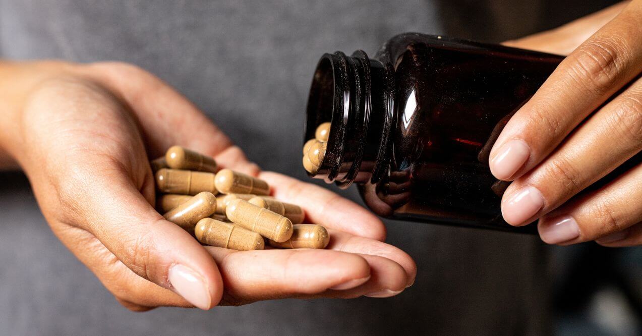 Hand holding ashwagandha capsules from a dark bottle