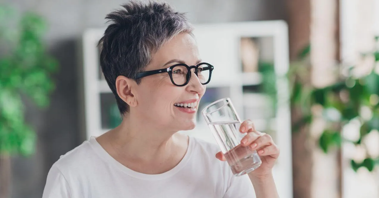 Smiling woman drinking pure water at home.