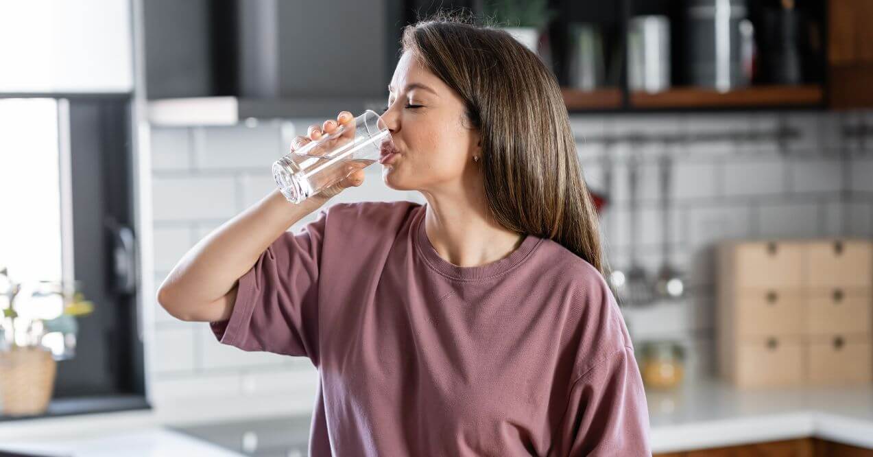 Woman drinking a glass of water in a modern kitchen setting.