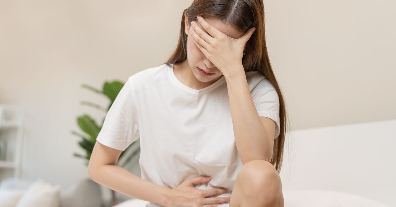 Woman experiencing abdominal pain while sitting on a bed.