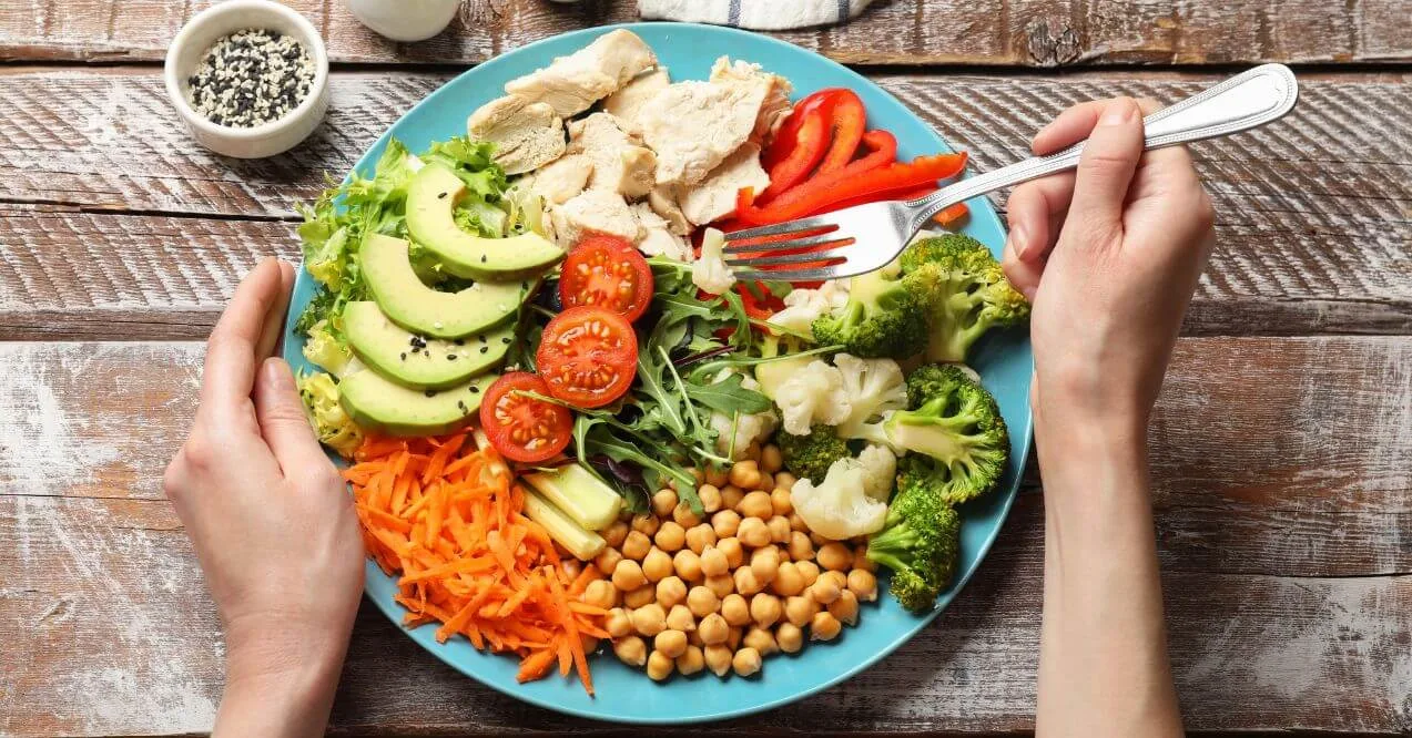 Colorful salad plate with vegetables, chickpeas, and chicken on a wooden table.