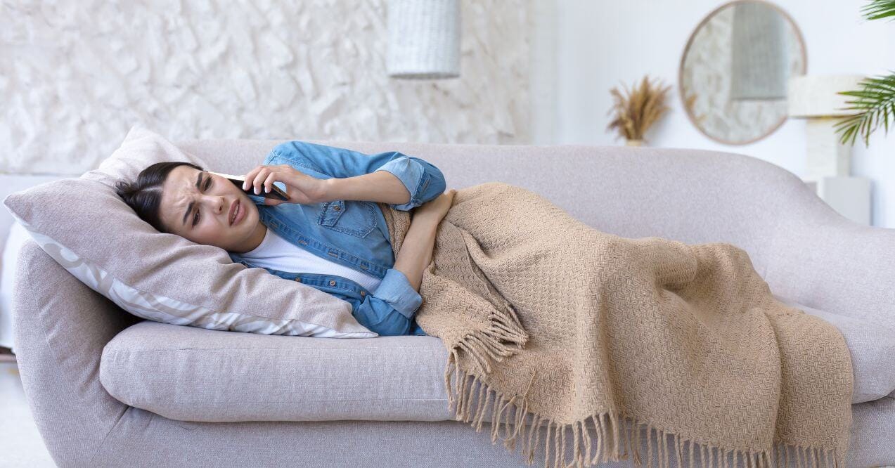 Woman lying on couch holding stomach while on the phone thinking how to restore gut health after stomach flu.