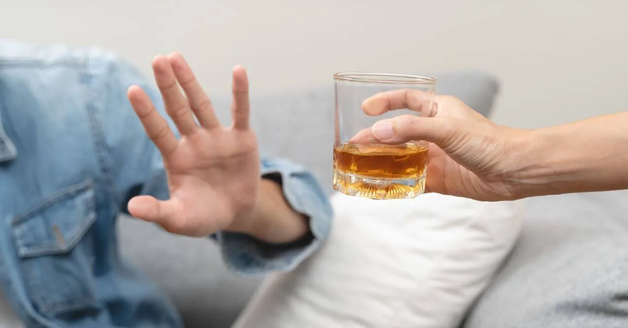 Person refusing a glass of whiskey with an open hand gesture.