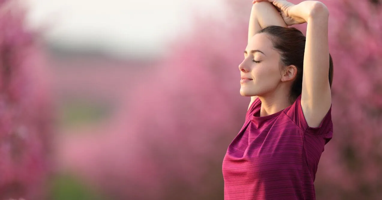 Woman stretching outdoors surrounded by blooming pink flowers in nature.