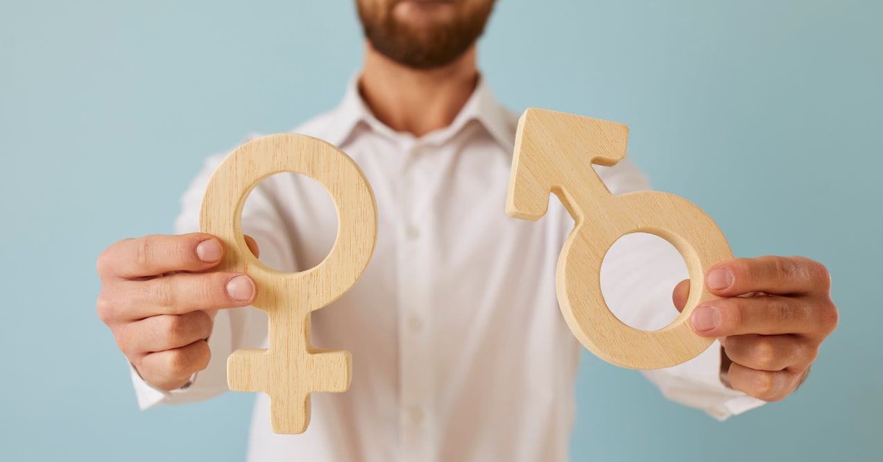 Man holding wooden male and female gender symbols in both hands against a light blue background.