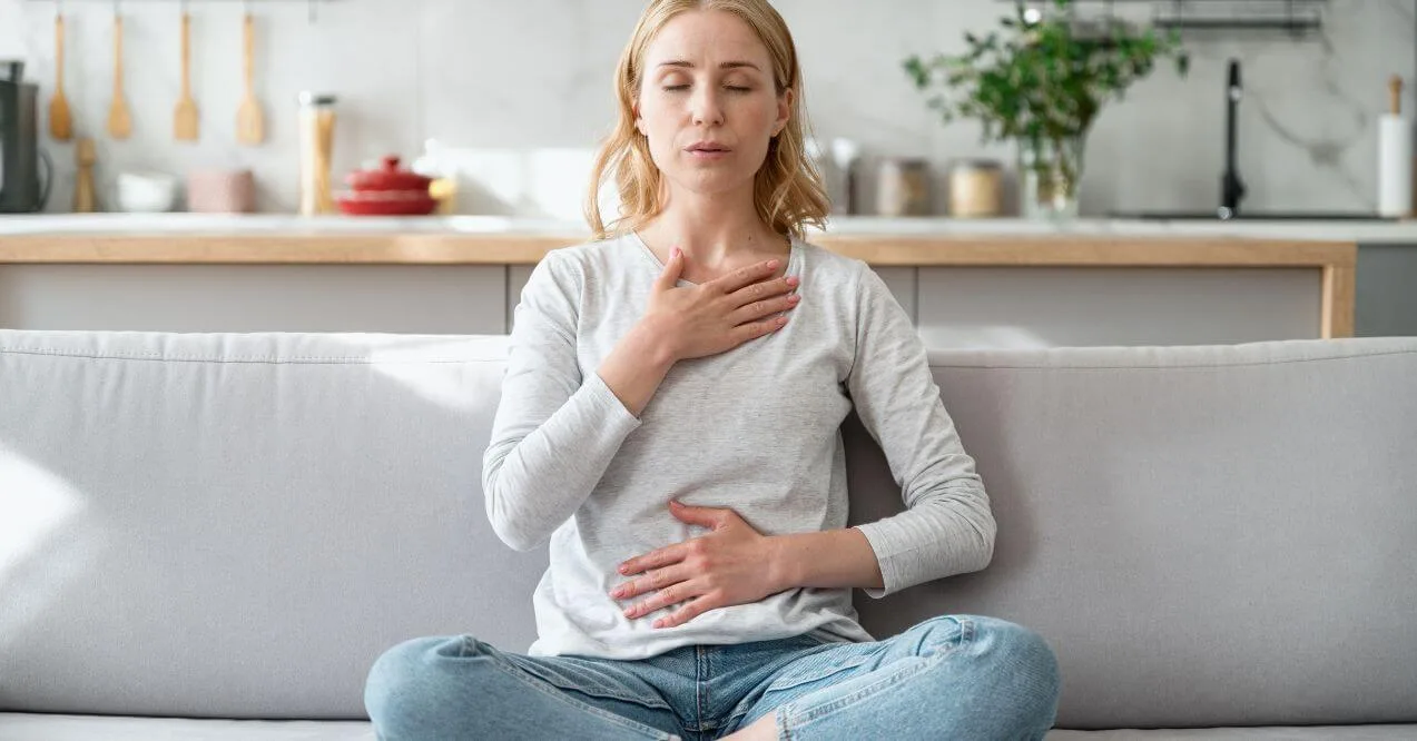 Woman practicing deep breathing while sitting on a sofa in a calm home environment.