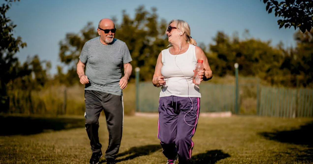 Senior couple jogging outdoors with smiles, holding water bottles.