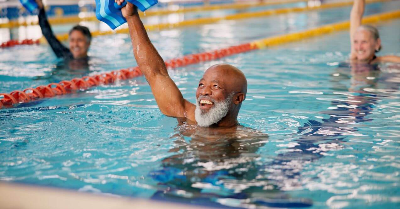 Elderly man smiling while doing water aerobics in a swimming pool.