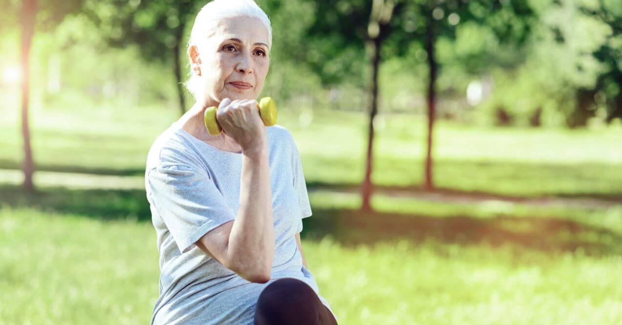 Elderly woman lifting dumbbell outdoors for exercise.