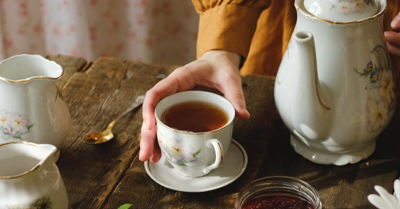 Pouring a cup of tea in a classic floral teacup on a wooden table.